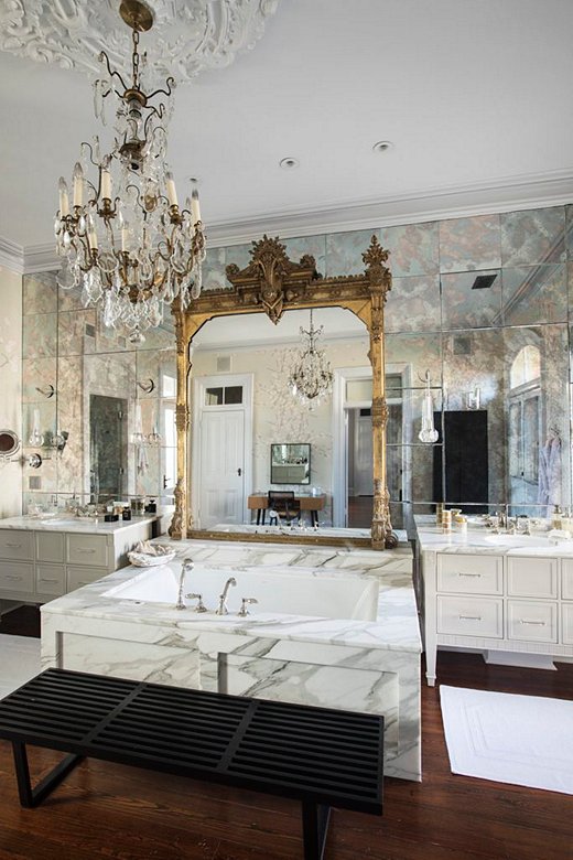 A stately 19th-century Eastlake mirror and an antique French chandelier add romance and glamour to the master bathroom, providing compelling counterpoints to the coolness of the gleaming marble walls and tub. The vintage George Nelson bench offers both practicality and a sleek Mid-Century Modern touch.
